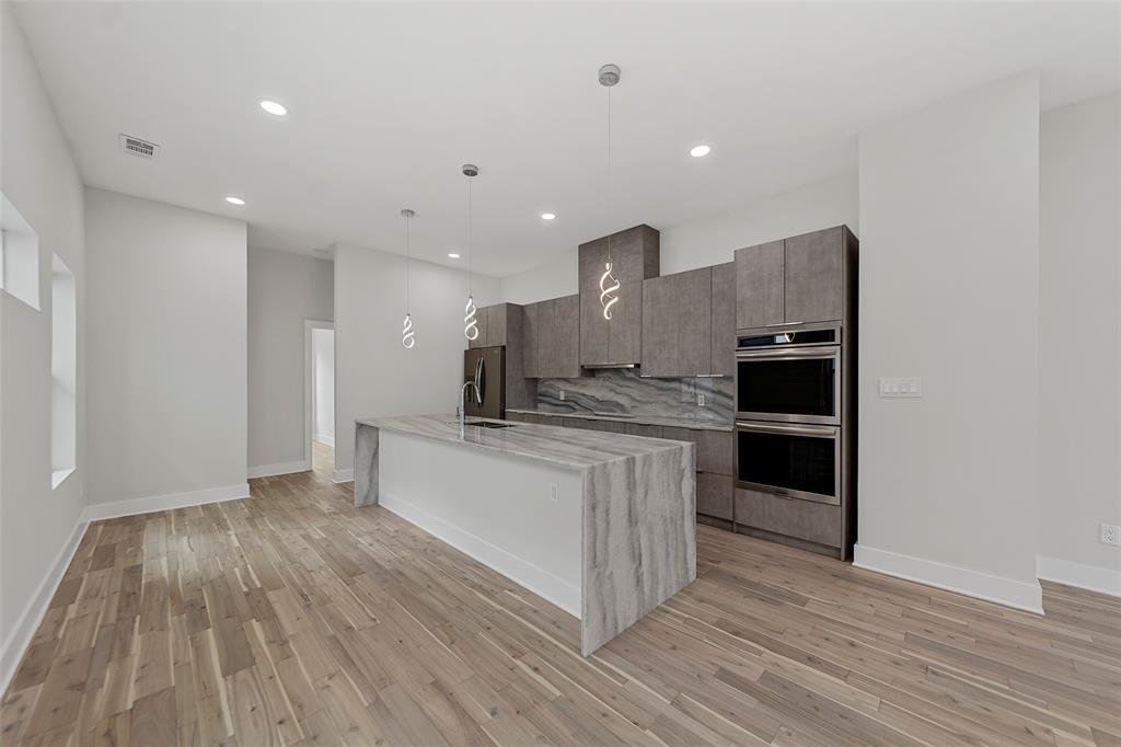 Kitchen featuring a waterfall-edge island, wood-finish flooring, recessed lighting, double wall ovens, and custom cabinetry
