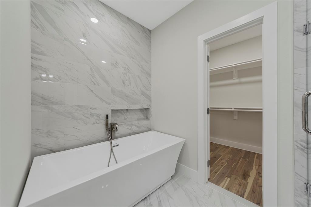 Freestanding soaking tub with polished chrome hand-held faucet, recessed wall niche, full-height decorative tile accent wall, and porcelain tile flooring