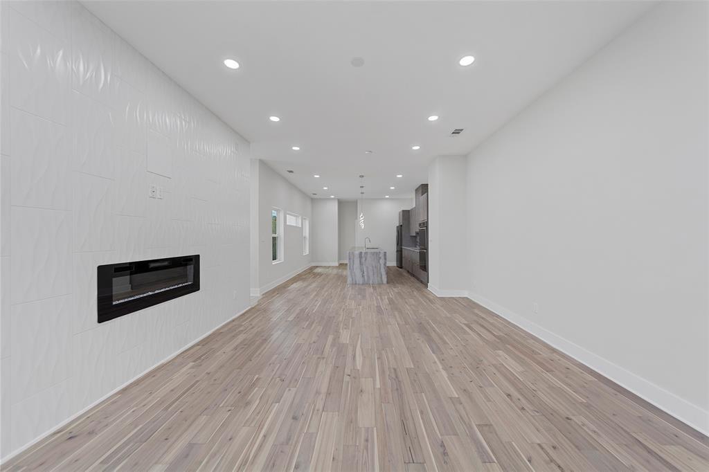 Open-concept interior featuring wood-finish flooring, recessed lighting, a built-in electric fireplace with a textured surround, and a center island with stone-finish surfaces