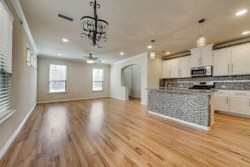 Kitchen with light hardwood / wood-style flooring, decorative light fixtures, ceiling fan with notable chandelier, stainless steel appliances, and white cabinetry