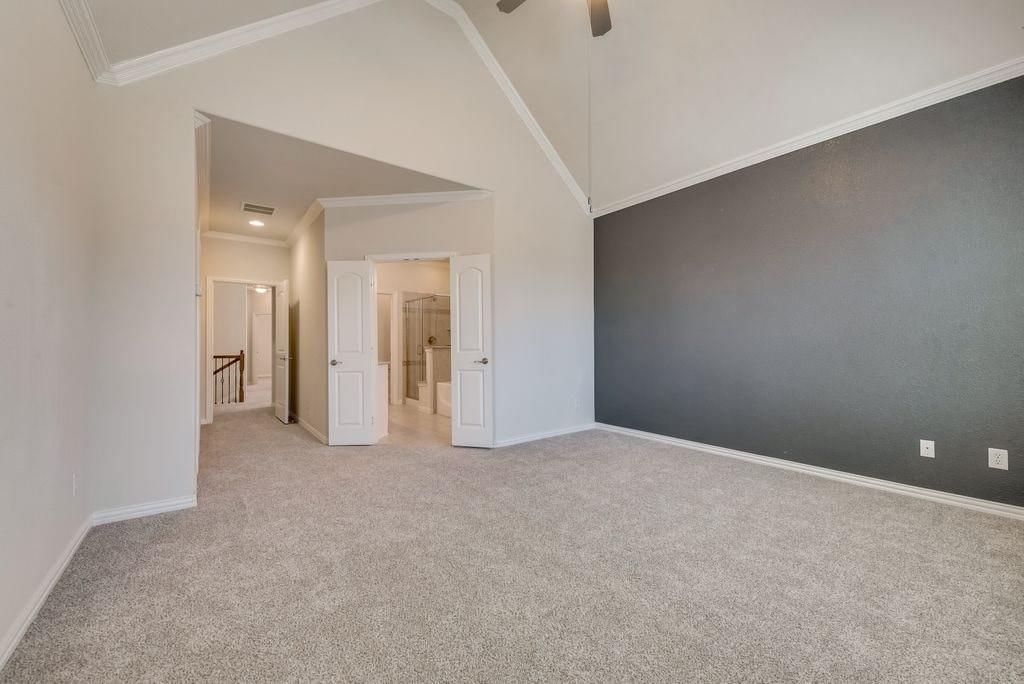 Carpeted empty room featuring crown molding, high vaulted ceiling, and ceiling fan