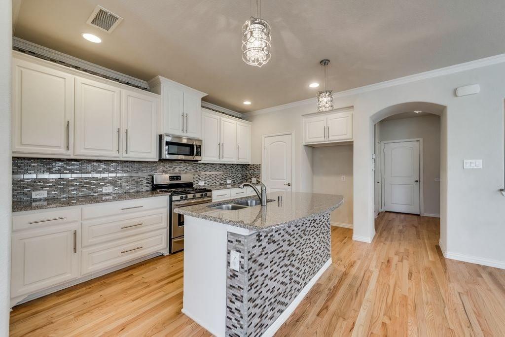 Kitchen featuring decorative light fixtures, a center island with sink, appliances with stainless steel finishes, white cabinetry, and light stone counters