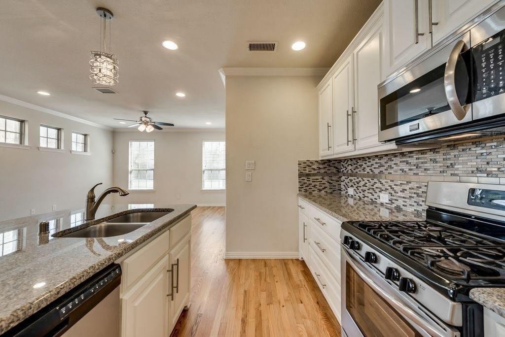 Kitchen with pendant lighting, sink, light stone countertops, appliances with stainless steel finishes, and white cabinets