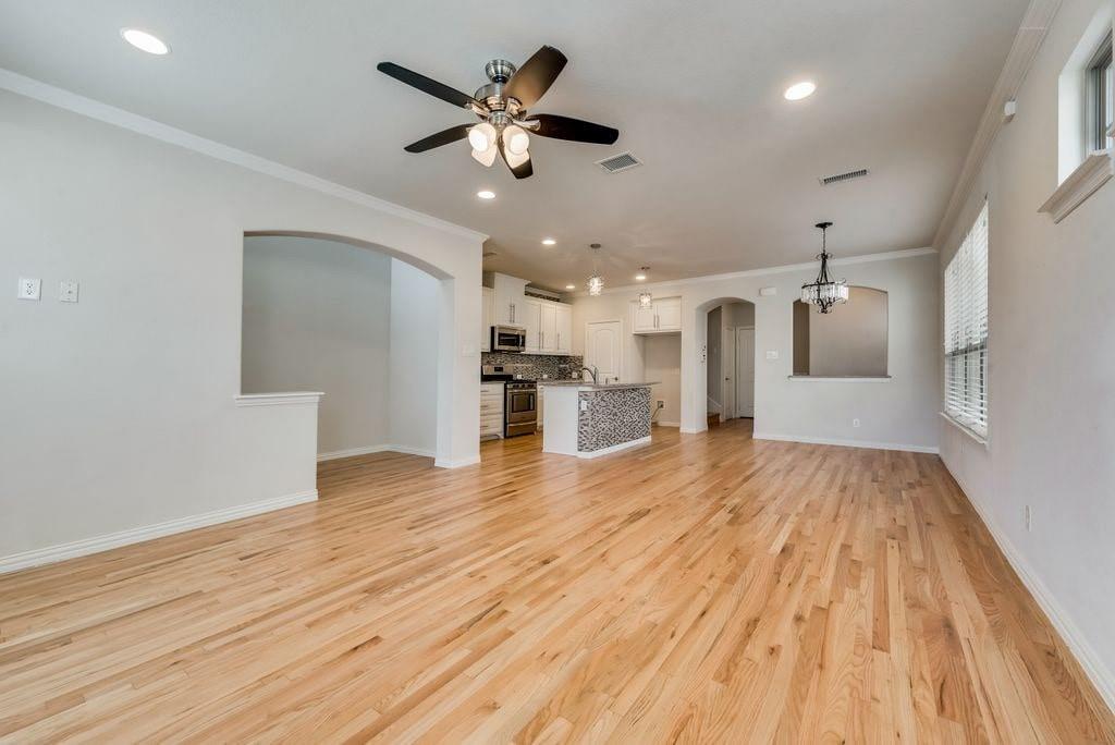 Unfurnished living room featuring plenty of natural light, ornamental molding, and ceiling fan with notable chandelier