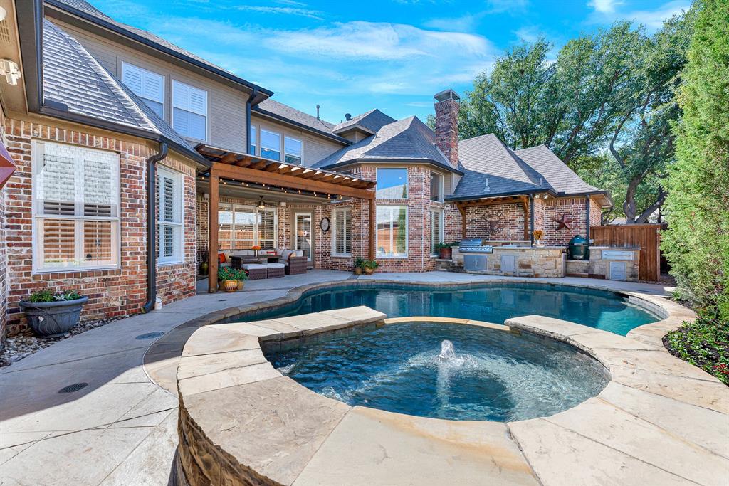 A central bubbling fountain water feature cascades gently over stone coping into the main pool basin. Picture listening to the soothing sound of flowing water as day turns to dusk across your private oasis.