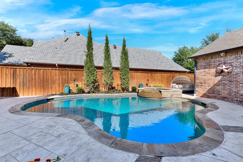 Freeform stone edging shapes a sparkling turquoise pool anchored by an elevated stone spa centerpiece. You will love taking an afternoon dip to cool off or relaxing in the spa under clear blue skies.