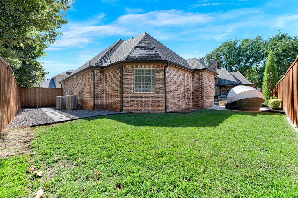 A neatly manicured lawn extends along the privacy-fenced border, highlighting the home's intricate rooflines and glass-block accent window. It is a wonderful space for pets to play freely or for enjoying quiet morning stretches outdoors.