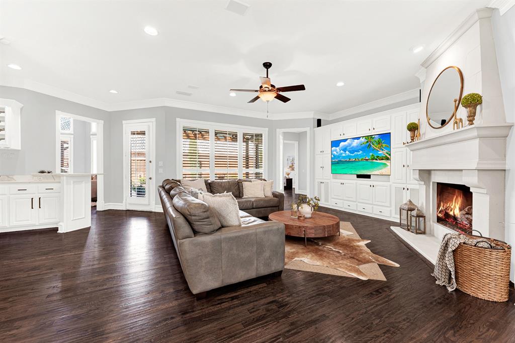A stately stone-look fireplace hearth anchors the far wall, framed by full-height custom entertainment cabinetry and expansive pool-facing windows. Imagine hosting weekend game days with family gathered together in the warm glow of the fire.