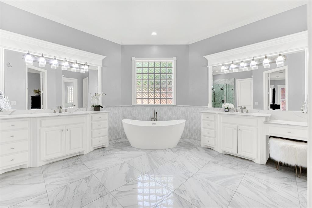 A sleek freestanding soaking tub serves as a sculpted centerpiece beneath a privacy-glass window, flanked by dual vanities. You will love treating yourself to a spa-like bath soak at night with gentle overhead vanity light gleaming across the polished tile.