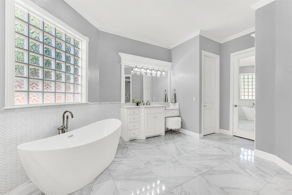 Custom built-in vanities include a lowered makeup station, highlighted by crisp trim detailing and large lighted mirrors. It is a serene environment to get ready effortlessly each morning surrounded by organized luxury.