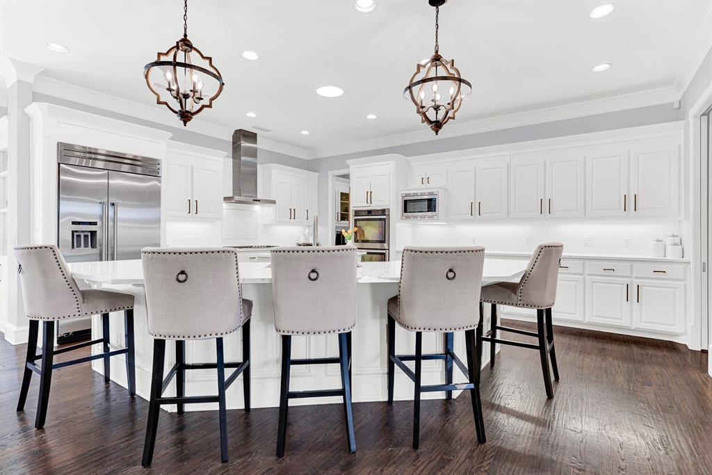 Sculpted lantern pendants cast a warm, welcoming light over the wide curved breakfast bar and custom white cabinetry. It is the perfect spot for casual weekday breakfasts or chatting with family while putting the finishing touches on a meal.