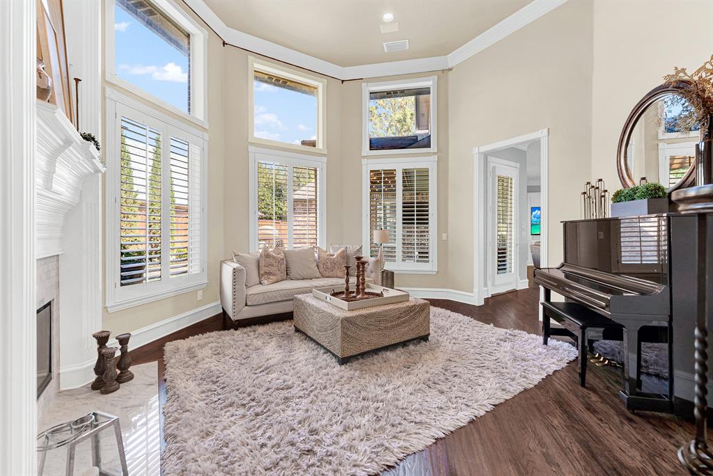 A dramatic two-story bay of shuttered windows creates a sun-drenched architectural focal point across the rich wood floors. Imagine unwinding with a chilled glass of wine while background piano tunes fill the airy, sunlit room.
