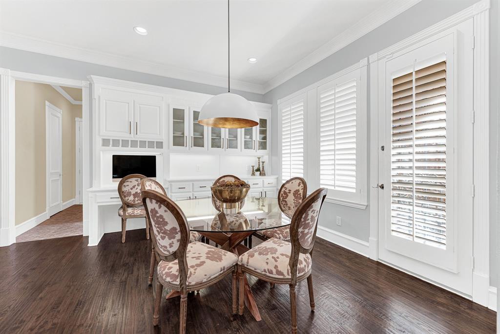 Plantation shutters filter soft morning sun across a custom office alcove and glass-front display cabinetry. Imagine starting your day checking early emails with a fresh cup of coffee right beside the sunny side yard view.