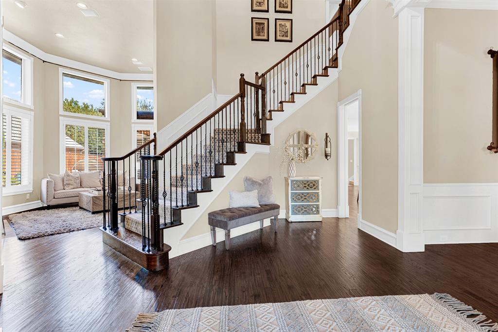 Rich hardwood floors anchor a dramatic open staircase that gracefully winds upward alongside towering high ceilings. Imagine returning home after a long day, kicking off your shoes, and relaxing as afternoon sunbeams stream through the grand windows