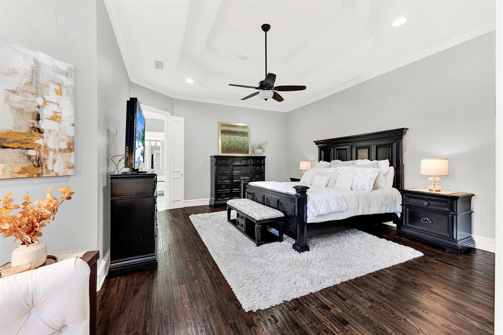 A multi-tiered tray ceiling adds architectural depth above, creating a grand sense of volume over rich, dark wood flooring. Picture sinking into fresh linens at the end of a long day, wrapped in quiet comfort and total peace.