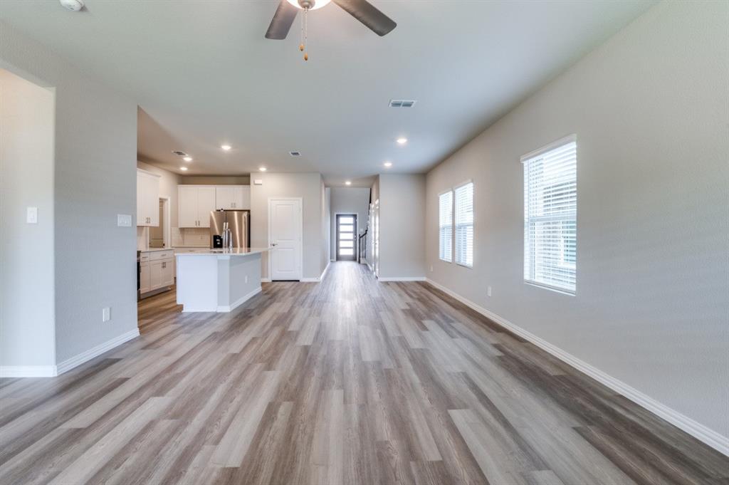 Open-concept interior featuring wood-finish flooring, recessed lighting, white cabinetry, a kitchen island with stone countertop, and large windows with blinds