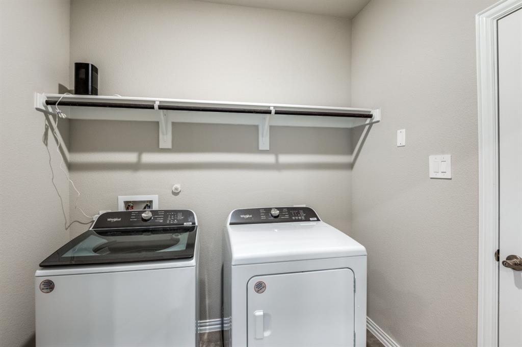 Utility area featuring neutral wall paint, white Whirlpool washer and dryer, and a built-in wall-mounted shelving unit with an integrated hanging rod