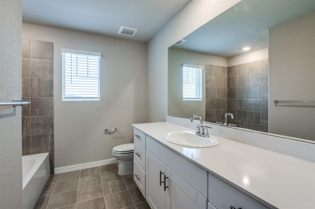 Bathroom featuring a white vanity with a solid surface countertop, an integrated oval sink, dark cabinetry hardware, large-format tile flooring, and a tiled tub surround