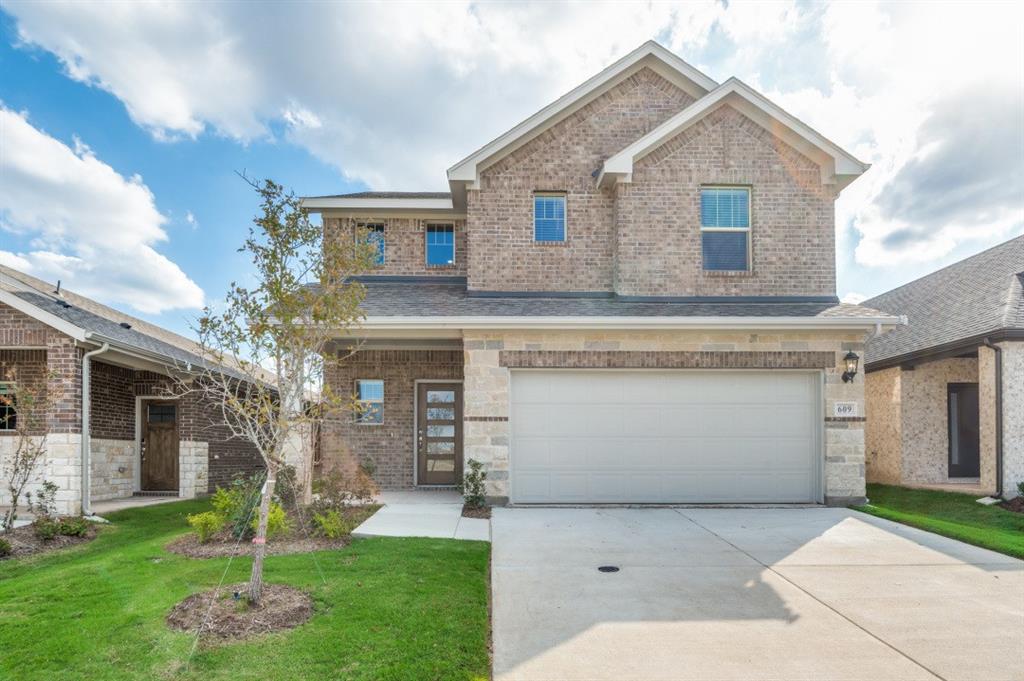 Two-story residence featuring a multi-textured brick and stone facade, covered entryway, attached two-car garage, and concrete driveway