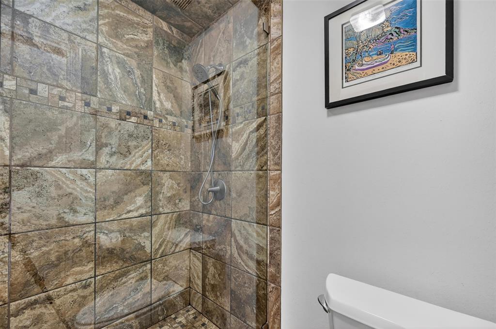 Walk-in shower featuring floor-to-ceiling stone-finish wall tiles, an integrated corner shelving unit, a frameless glass enclosure, and a handheld showerhead