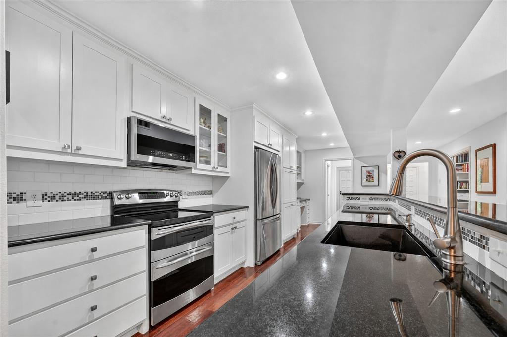 Kitchen featuring white shaker-style cabinetry, polished dark countertops, stainless steel appliances, subway tile backsplash with glass mosaic accents, and wood-finish flooring