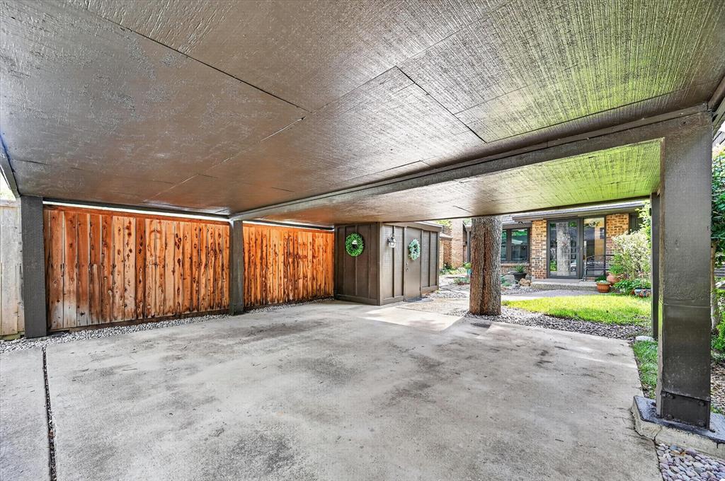 Covered parking structure featuring a concrete pad, vertical wood siding, and integrated exterior storage unit
