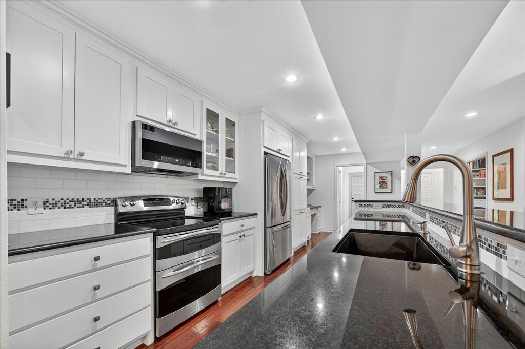 Kitchen featuring white shaker-style cabinetry, dark stone countertops, stainless steel appliances, a mosaic tile backsplash, and wood-finish flooring