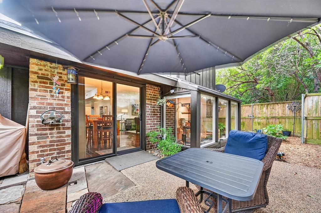 Patio featuring exposed brick exterior, sliding glass door, stone-finish paving, and wooden perimeter fencing