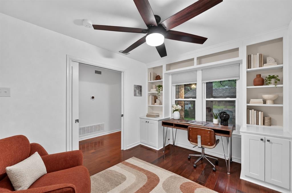 Custom built-in white cabinetry with integrated shelving, dark wood-finish flooring, and a multi-blade ceiling fan with central illumination