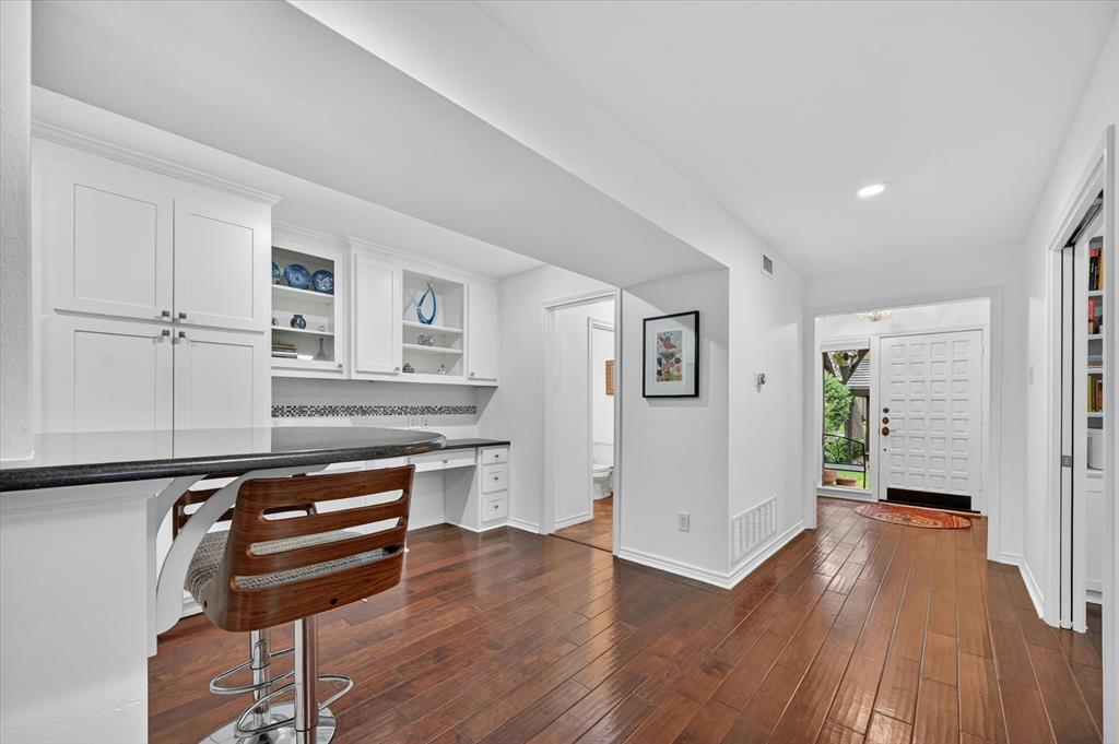 Built-in white cabinetry, integrated desk workspace, dark solid-surface countertop, and wood-finish flooring