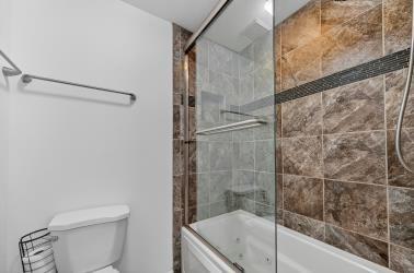 Walk-in shower enclosure featuring floor-to-ceiling neutral tile, a built-in recessed shelf, a glass sliding door, and integrated jetted tub