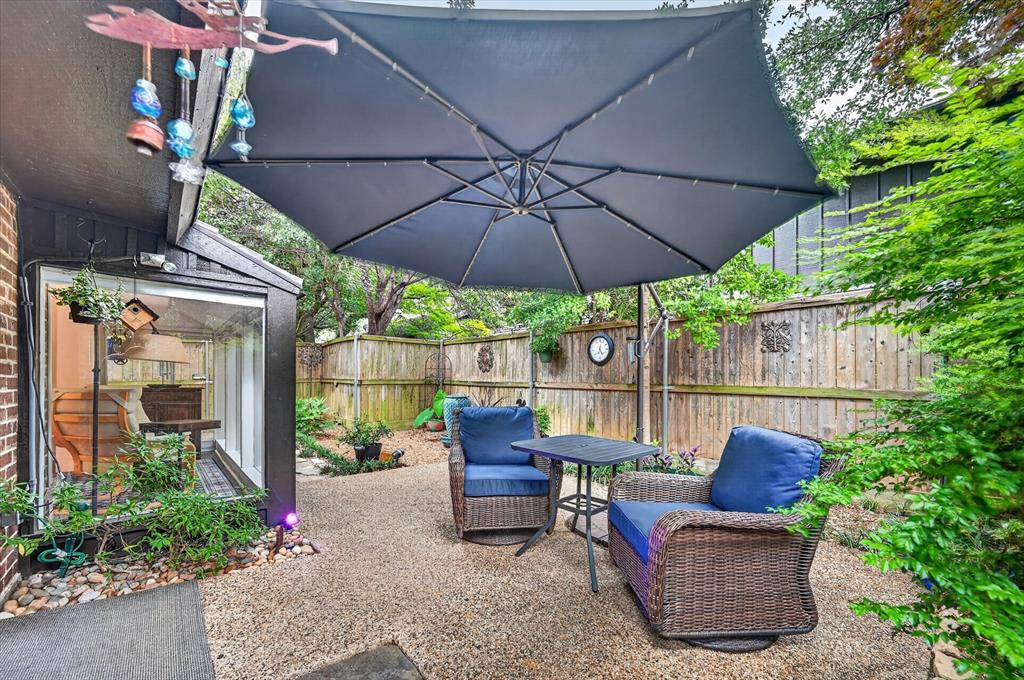 Enclosed patio featuring exposed aggregate hardscaping, wood privacy fencing, and exterior wall-mounted lighting