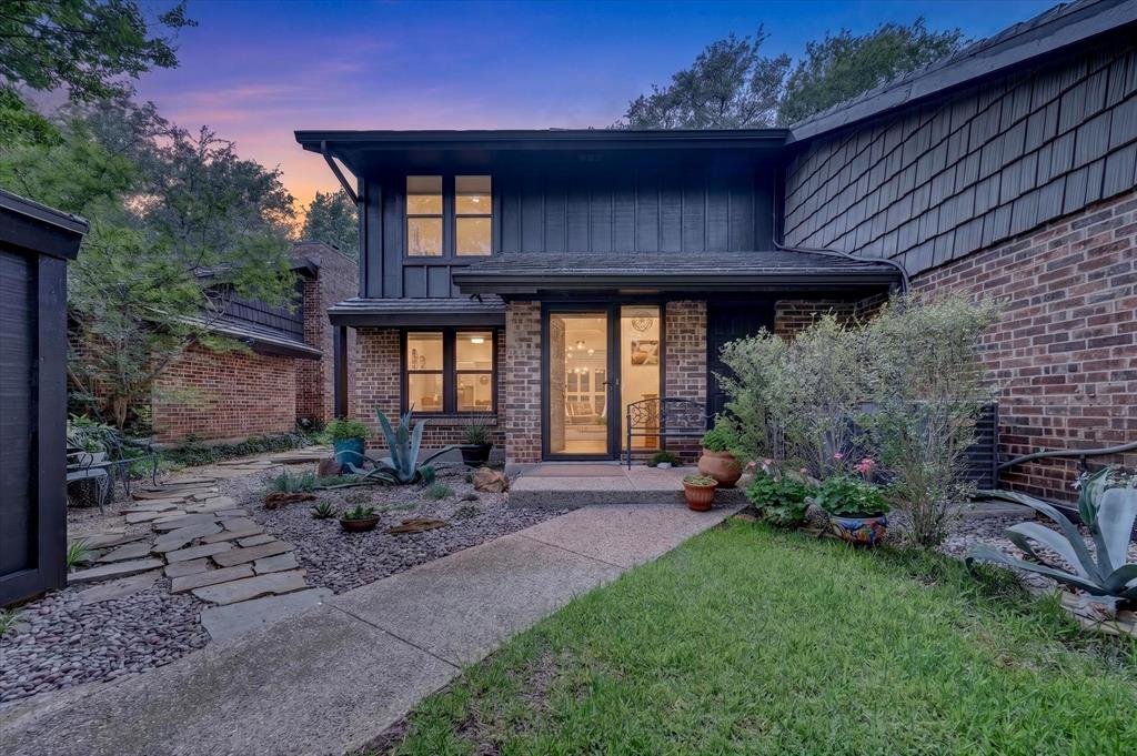 Multi-level exterior featuring a combination of brick and vertical siding, stone-paved walkway, xeriscaped garden beds, and expansive multi-pane windows Multi-level exterior featuring a combination of brick and vertical siding, stone-paved walkway, xeriscaped garden beds, and expansive multi-pane windows