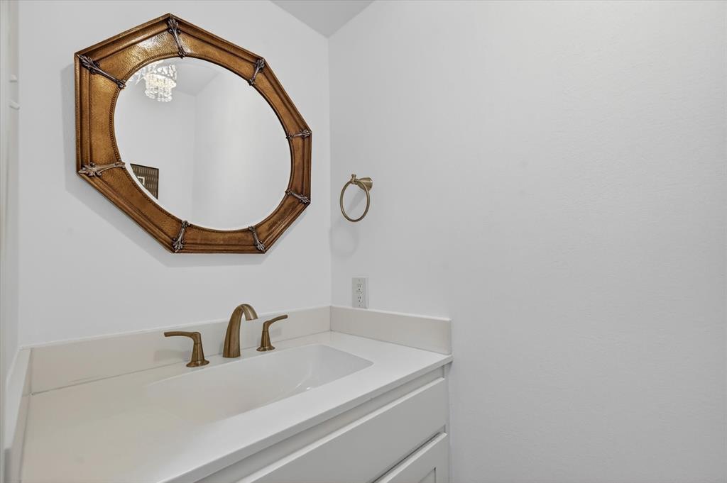 Solid surface vanity with an integrated basin, brass-finish widespread faucet, wall-mounted circular decorative mirror, and circular towel ring