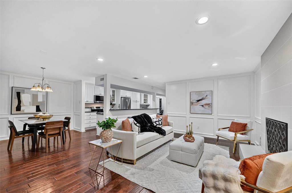 Open-concept living space featuring wood-finish flooring, recessed lighting, white wainscoting, and a fireplace with a geometric-patterned metal screen