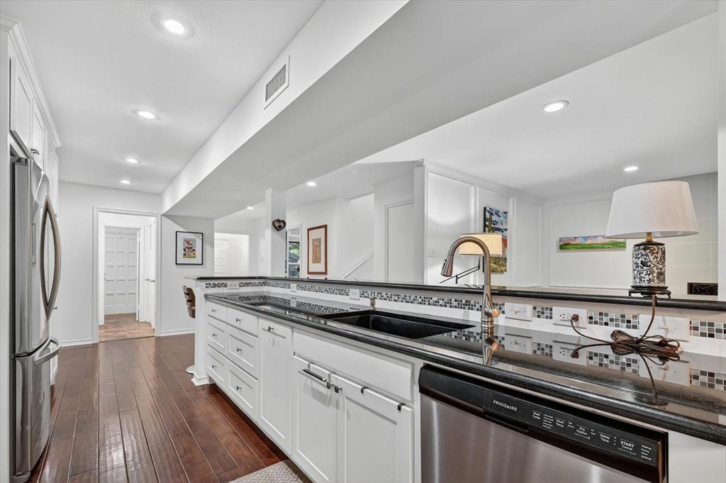 Kitchen featuring white shaker-style cabinetry, dark stone countertops, mosaic tile backsplash, integrated stainless steel appliances, and wood-finish flooring