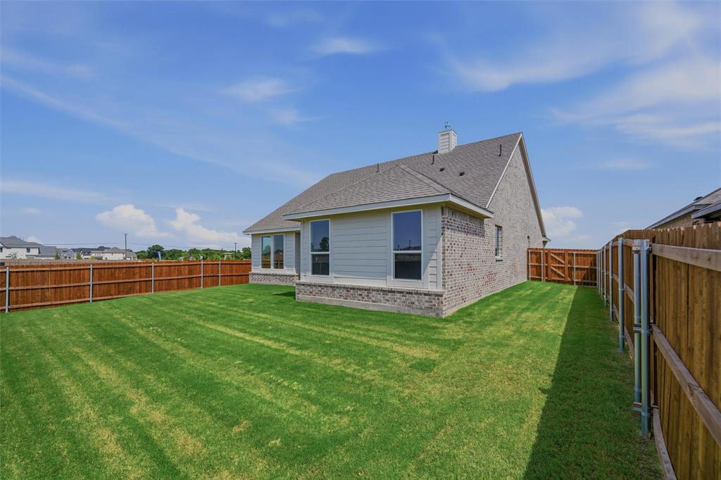 Expansive rear yard with a manicured lawn, full wood fencing, and a side gate