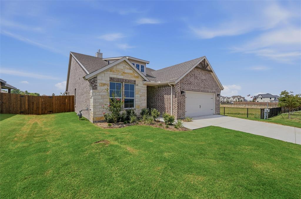 Brick exterior with stone accents, attached garage, concrete driveway, and a wood privacy fence