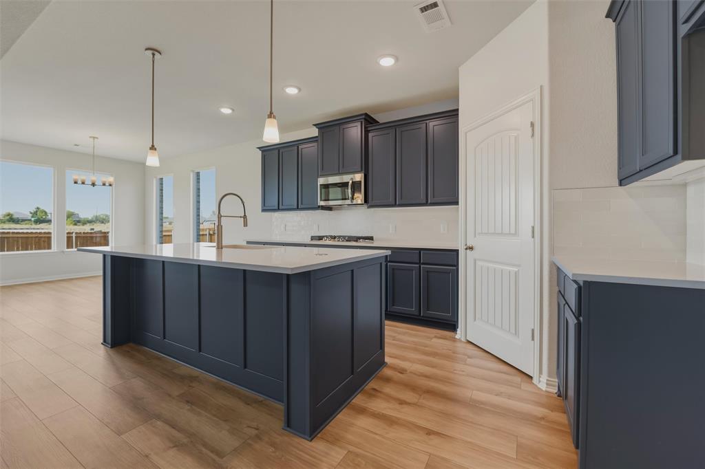 Kitchen featuring a center island, dark cabinetry, light countertops, stainless steel appliances, and wood-finish flooring