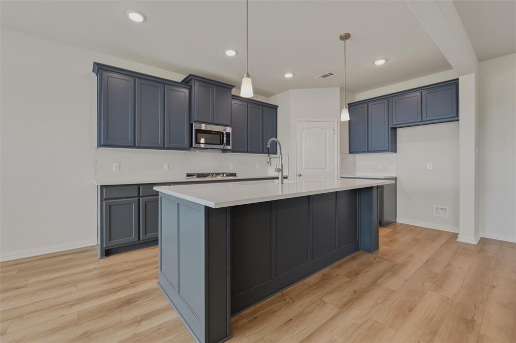Kitchen featuring wood-finish flooring, dark cabinetry, light countertops, stainless steel appliances, and a central island with an integrated sink