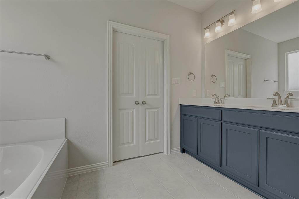 Dual-sink vanity with blue cabinetry and white countertops, large wall-mounted mirror, and a built-in bathtub