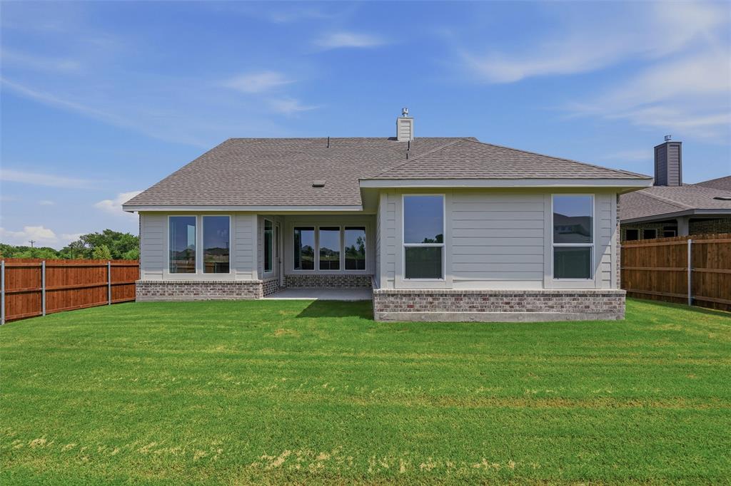 Expansive backyard featuring a manicured lawn, wood fencing, and a covered patio