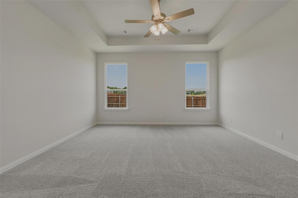 Tray ceiling with a ceiling fan, two windows, and gray carpeting