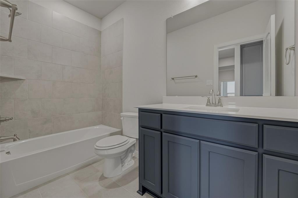 Tub-shower combination with tiled surround, built-in shelving, and a vanity featuring a single sink and cabinet storage