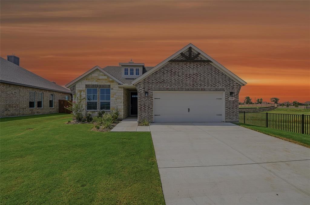Brick and stone facade, dormer window, attached garage, concrete driveway, and a black wrought iron fence Brick and stone facade, dormer window, attached garage, concrete driveway, and a black wrought iron fence