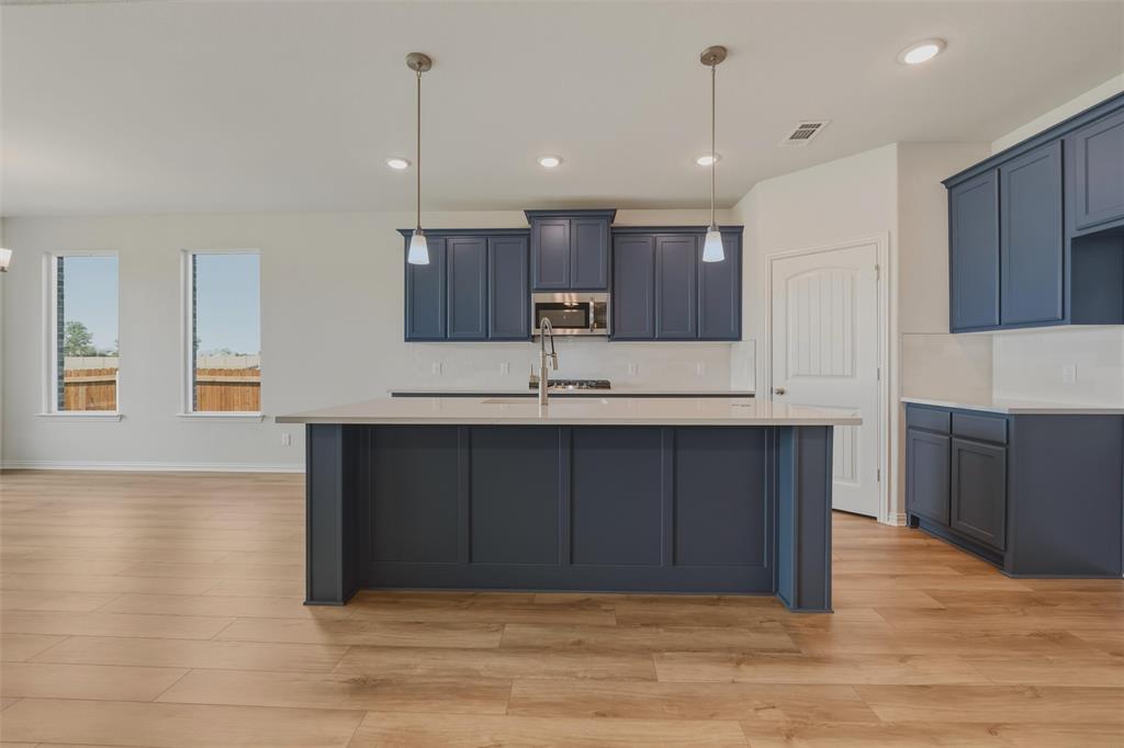 Kitchen featuring wood-finish flooring, an island with pendant lighting, stainless steel appliances, and white subway tile backsplash