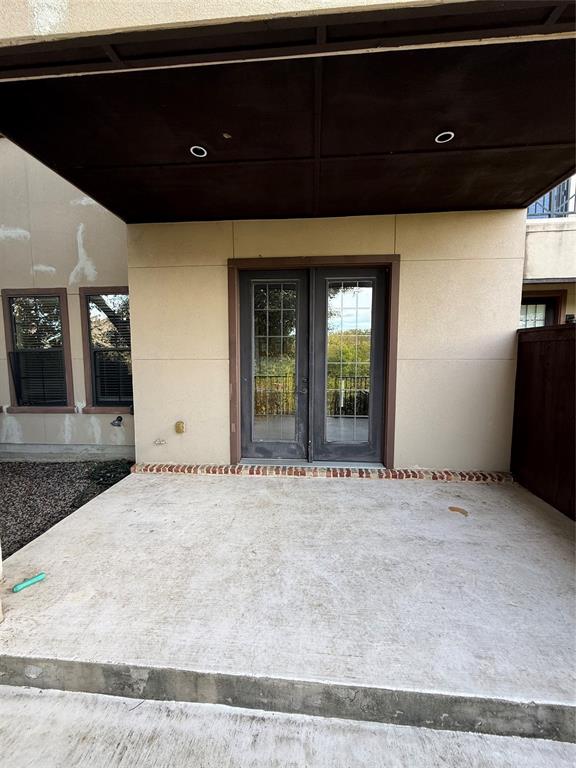 Covered concrete patio featuring a brick threshold, dual French doors with multi-pane glass, and recessed ceiling lighting