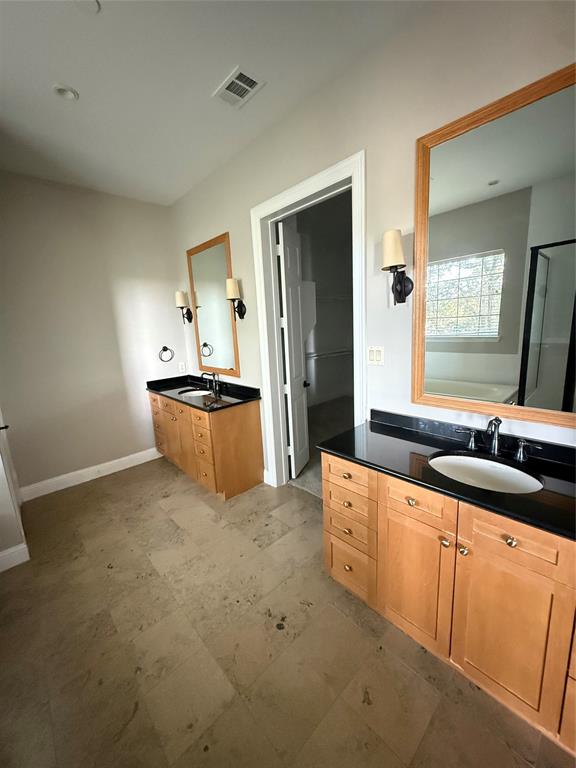 Dual wooden cabinetry vanities with dark stone countertops, undermount sinks, framed mirrors, and wall-mounted light fixtures, finished with large-format tile flooring