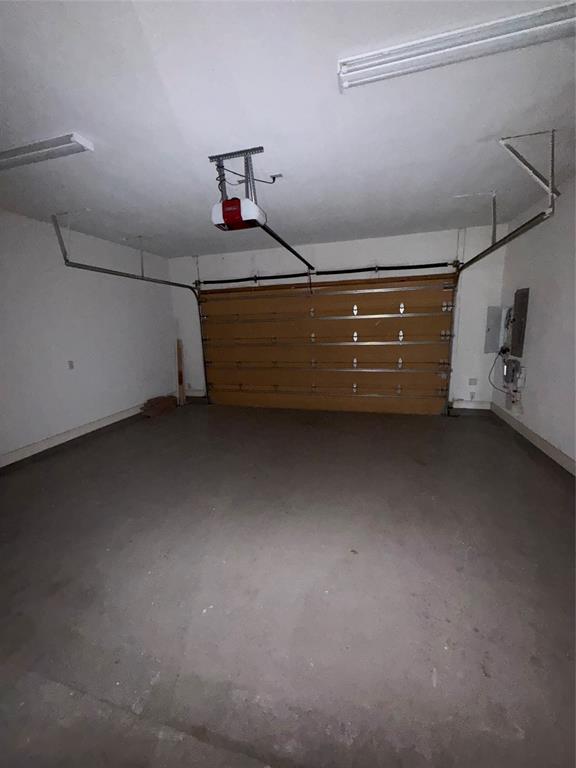 Two-car garage featuring a sectional metal garage door, automated ceiling-mounted opener, concrete flooring, and overhead fluorescent lighting