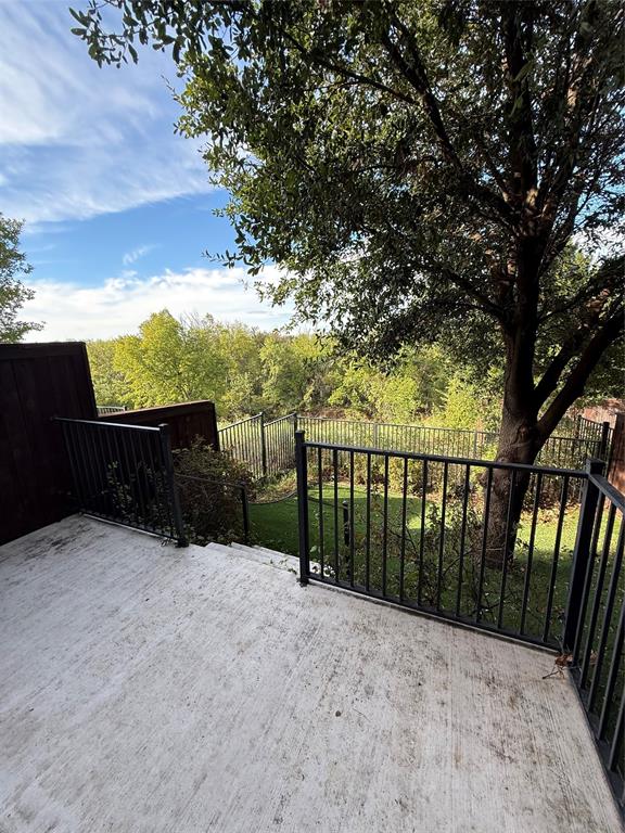 Concrete patio featuring a black metal railing, wood privacy fencing, and a mature tree